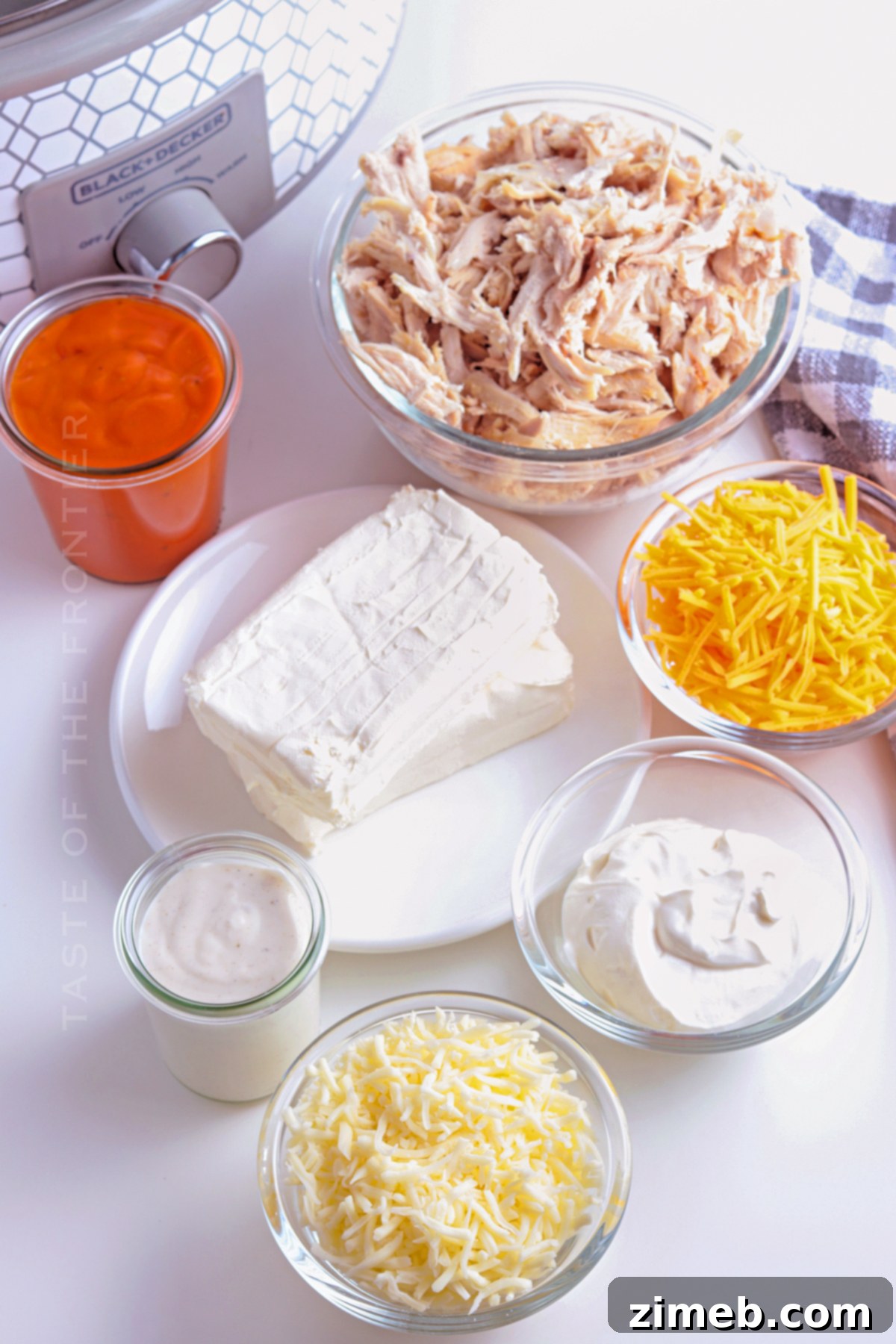 Crock-Pot Buffalo Chicken Party Dip 4 A collection of fresh ingredients laid out for Slow Cooker Buffalo Chicken Dip, including cream cheese, shredded chicken, buffalo sauce, ranch dressing, sour cream, and various cheeses.