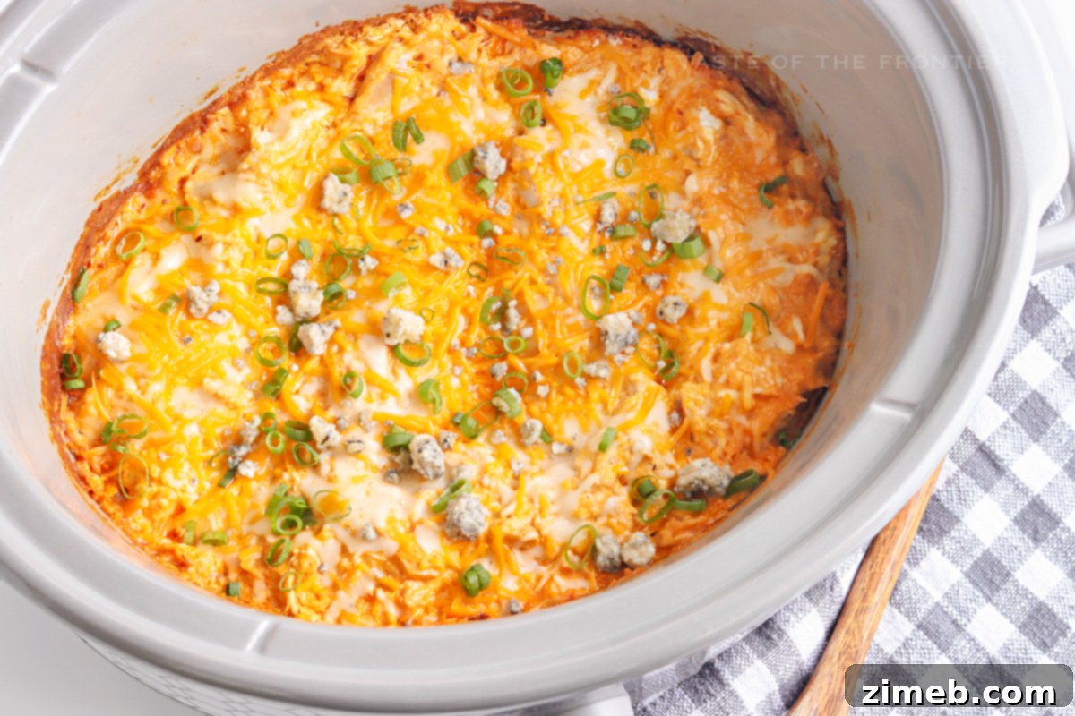 Crock-Pot Buffalo Chicken Party Dip 8 Game Day Slow Cooker Dip in a decorative crock pot, garnished with blue cheese and green onions, with chips around it.