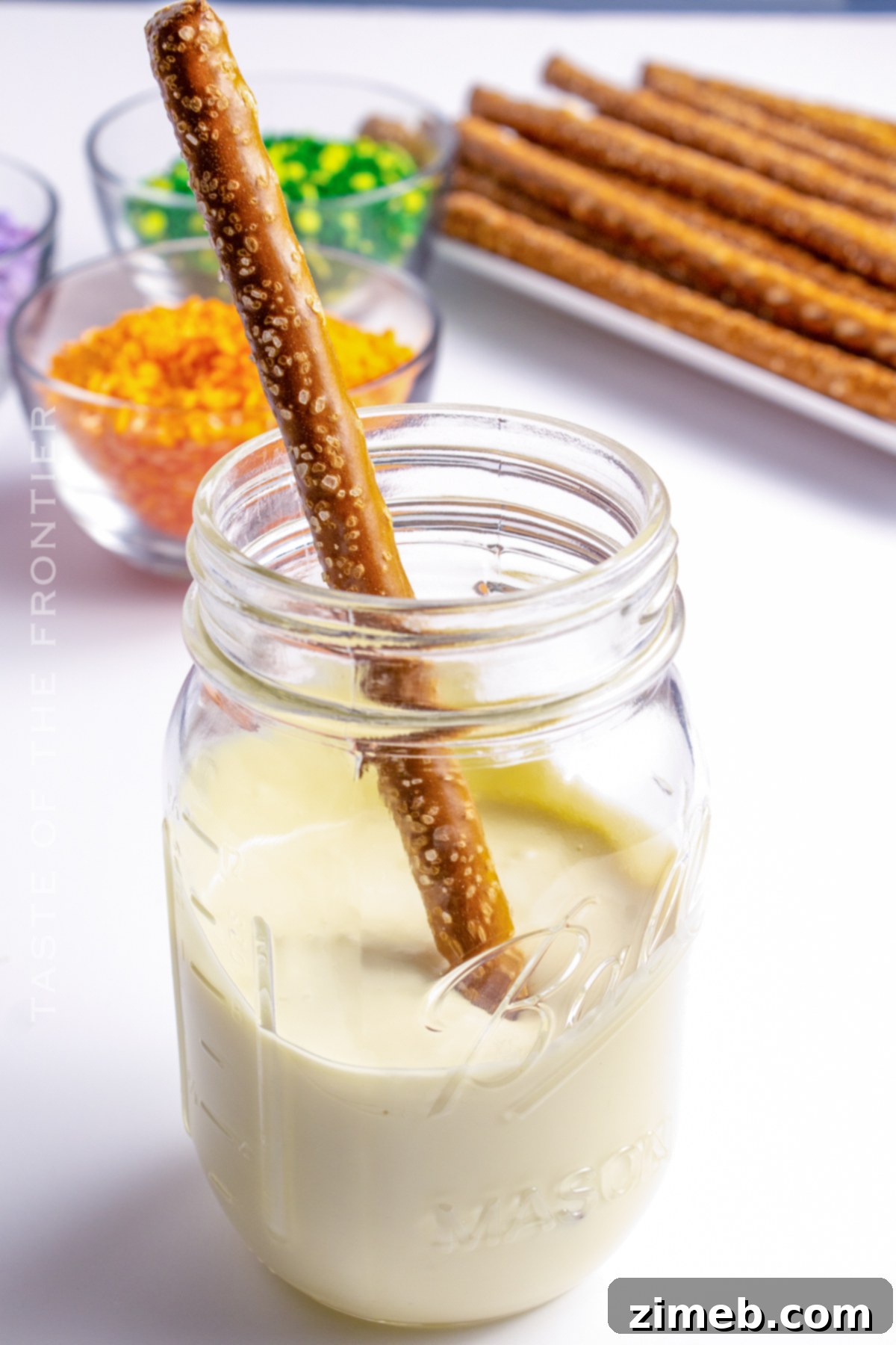 A hand dipping a pretzel rod into melted white chocolate, demonstrating how to make Halloween Pretzels