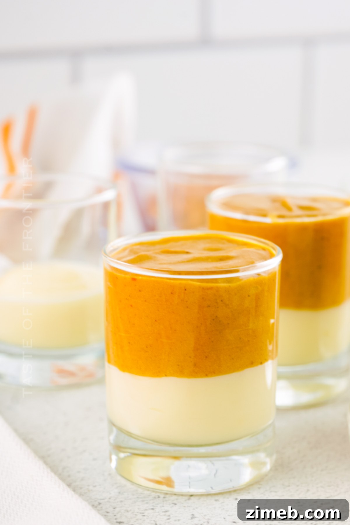 Close-up of shot glasses being filled with creamy pudding mixture, demonstrating the filling technique.
