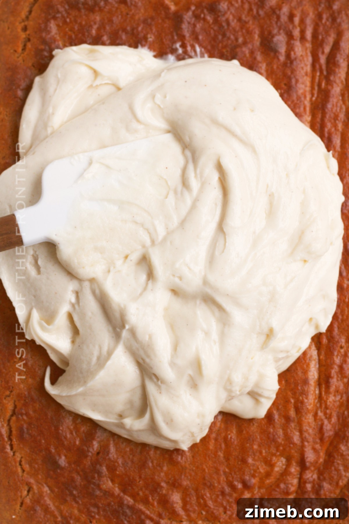 Applying cream cheese frosting to a homemade pumpkin spice cake.
