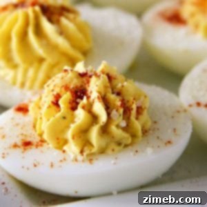 Close-up of traditional deviled eggs, halved and filled with a smooth, creamy yolk mixture, garnished with a sprinkle of paprika, arranged neatly on a plate.