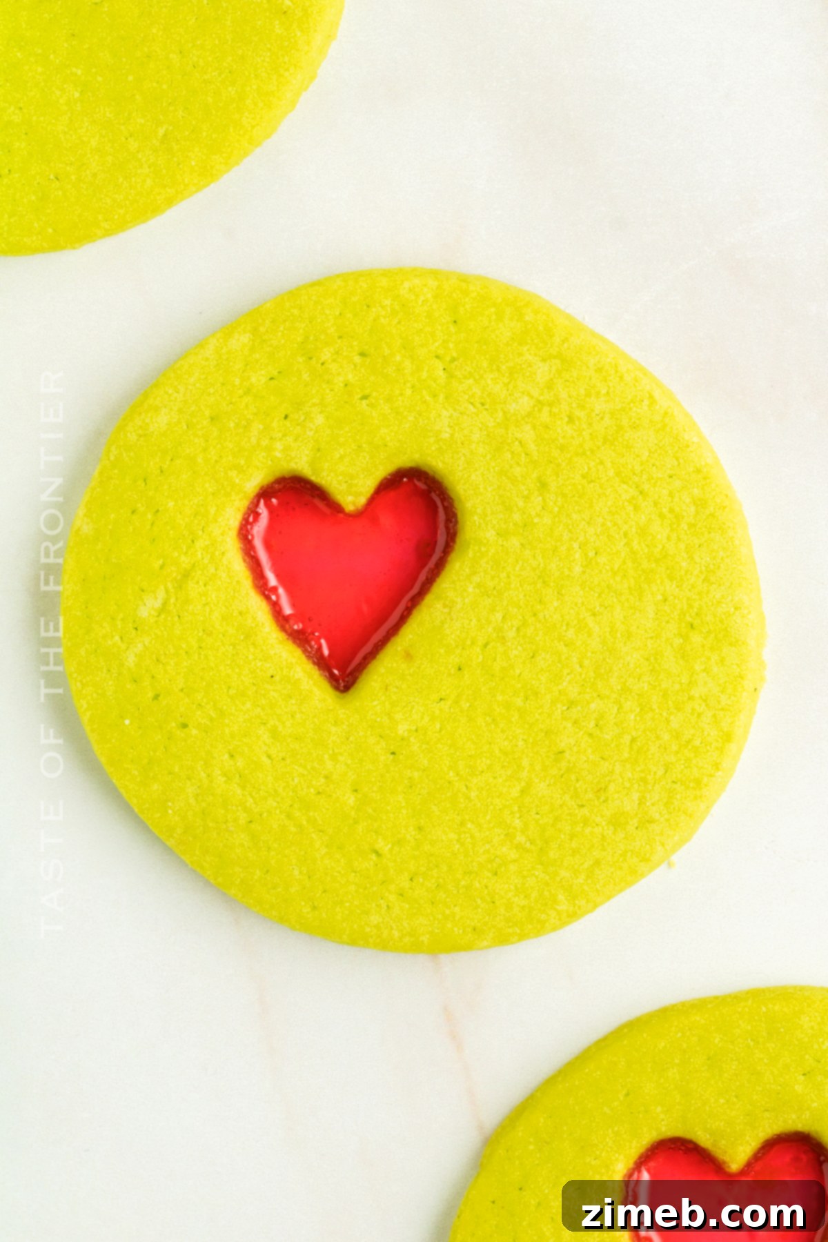 Close-up of vibrant green cookies with a sparkling red heart candy center, reminiscent of the Grinch.