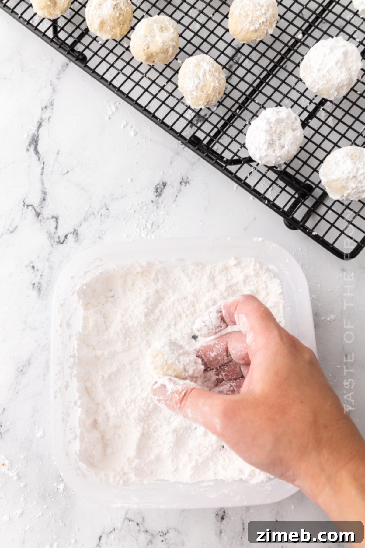 Mexican Wedding Cookies being rolled in powdered sugar for their signature finish.
