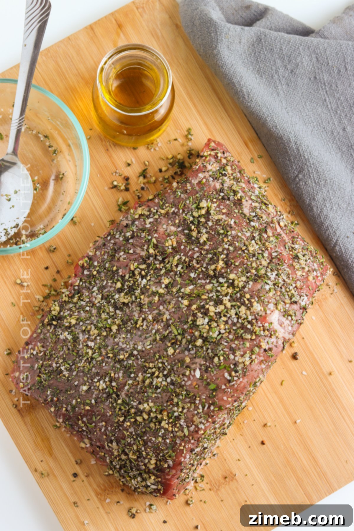 Close-up of a rump roast being seasoned generously with herbs and spices for roasting.