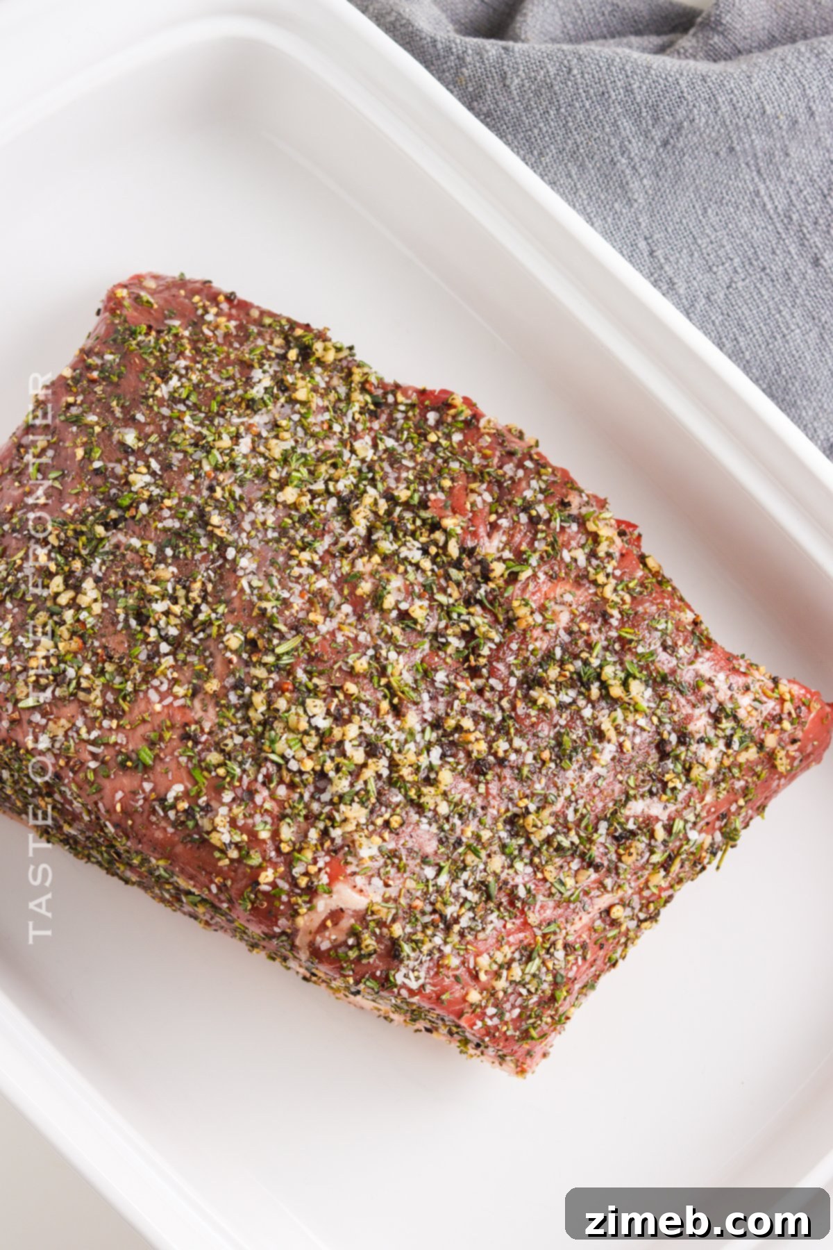 Oven roast beef seasoned and ready to be placed in the oven, sitting in a roasting pan.