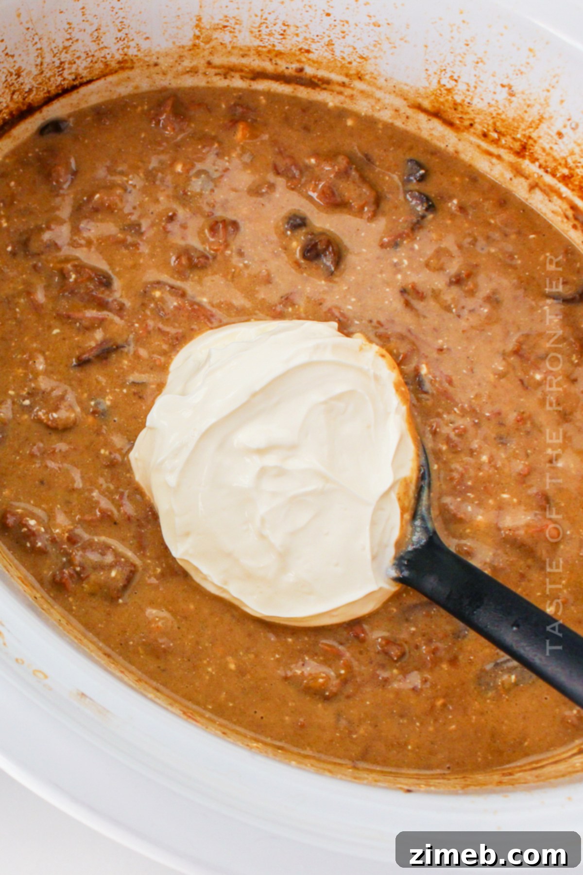 Cozy Comfort Slow Cooker Beef Stroganoff 8 Adding sour cream to creamy beef stroganoff in a slow cooker for the finishing touch.