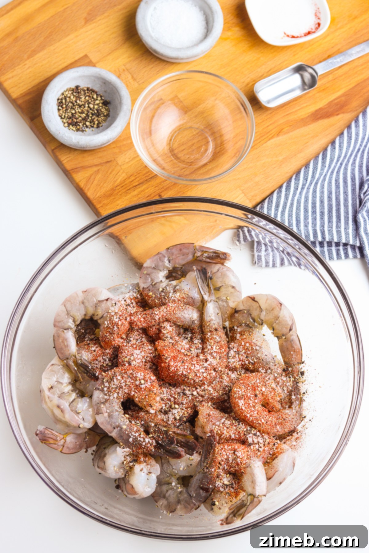 Savory Smoked Shrimp 5 A hand adding a mix of seasonings onto raw shrimp in a bowl, preparing them for smoking.
