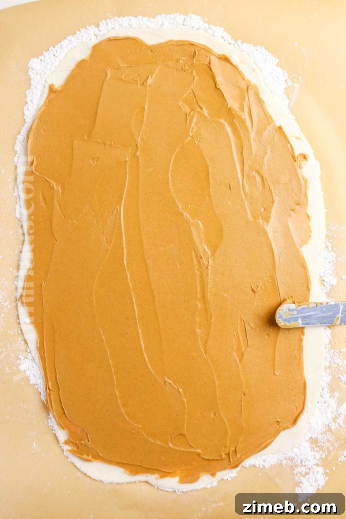 Potato Truffles 6 Spreading creamy peanut butter evenly over a rolled-out potato candy dough, leaving a small border.