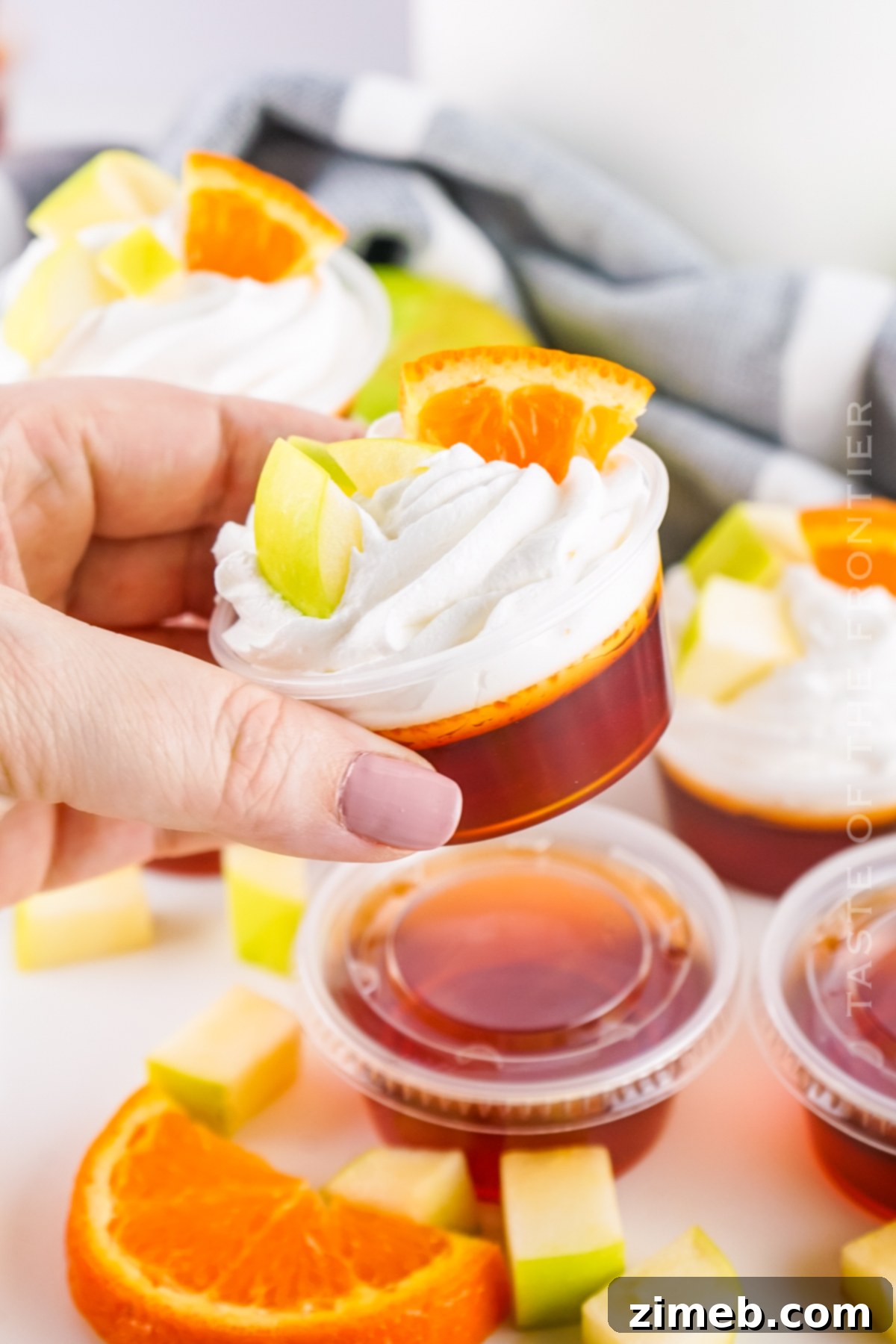 Individual Sangria Jello Shots in clear plastic cups, garnished with fruit and whipped cream.